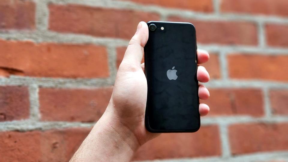 hand holding black iphone se against a brick wall