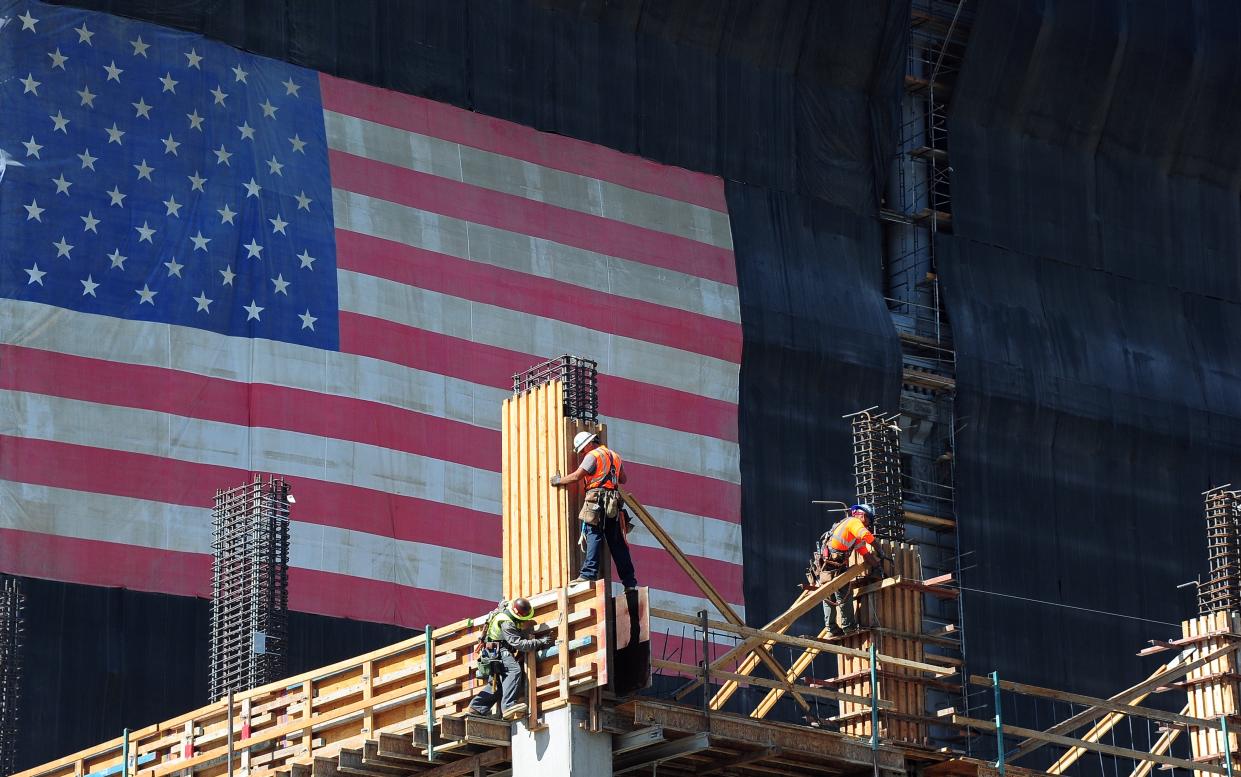 Construction workers work on the construction of a new building partially covered with a large American flag on September 25, 2013 in Los Angeles, California, where the state's governor, Jerry Brown, signed a law that will increase the minimum wage of California from $8 to $10 per hour by 2016. AFP PHOTO/Frederic J. BROWN (photo credit should read FREDERIC J. BROWN/AFP via Getty Images)