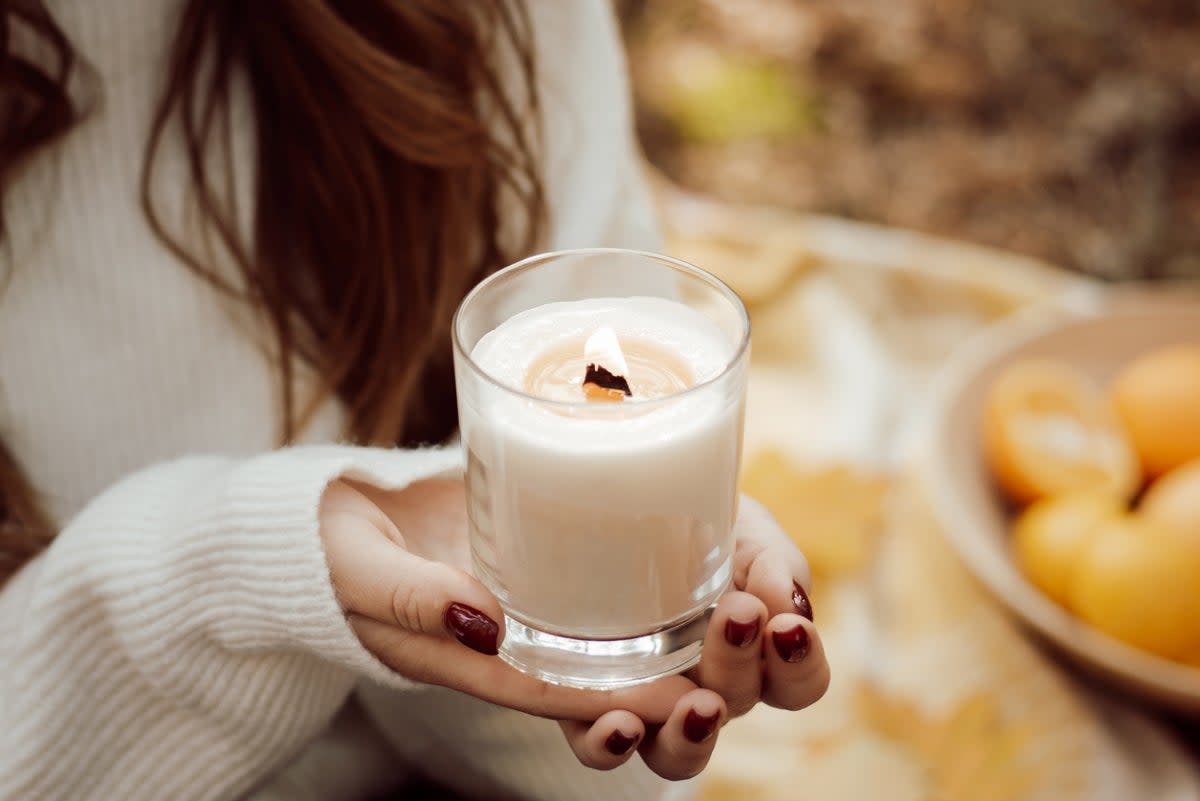 Woman holding lit white candle in hands.