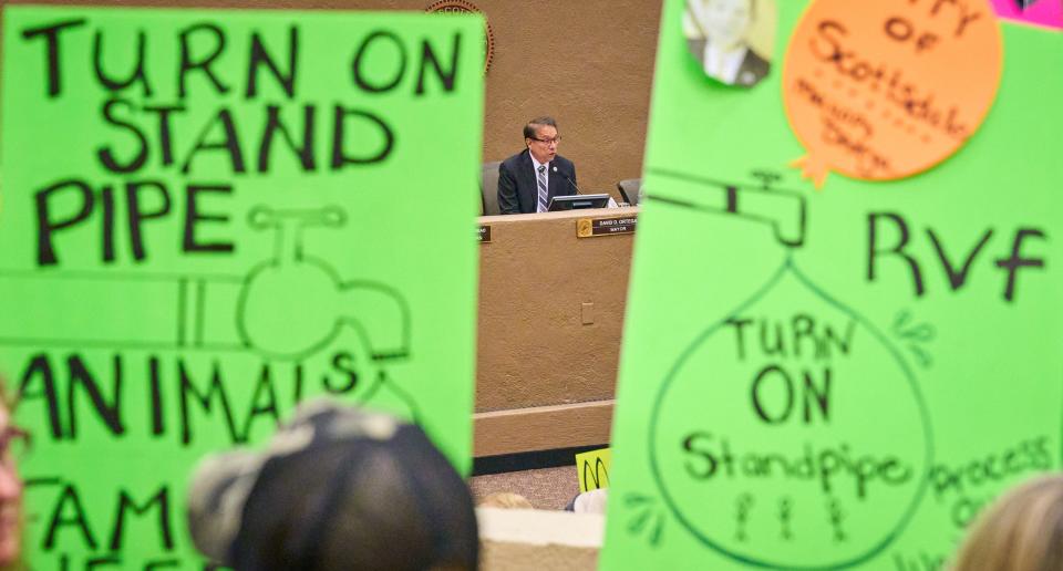 As residents of the Rio Verde Foothills hold signs calling on Scottsdale mayor David Ortega to turn on the standpipe, mayor Ortega listens to public comments during a Scottsdale city council meeting at the Scottsdale Civic Center on Tuesday, Jan. 10, 2023.
