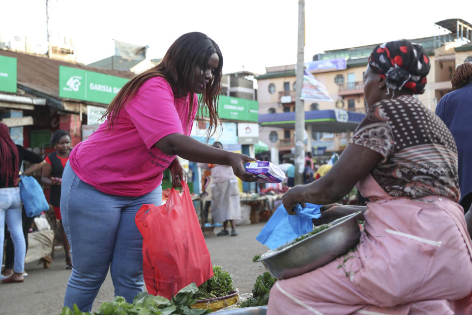 Lorna Mweu, left, popularly known as Mamake Bobo, who founded Period Party, an organization that holds an annual event to help end stigma, distributes free sanitary pads to women while explaining to them the need to openly discuss menstruation with their daughters to end period shaming, in Kiambu market, Nairobi, Kenya Monday, March 6, 2023. Kenyan senator Gloria Orwoba has said that she attended parliament last month while wearing a white pantsuit stained by her menstruation in order to combat the stigma surrounding women's monthly periods. (AP Photo/Brian Inganga)