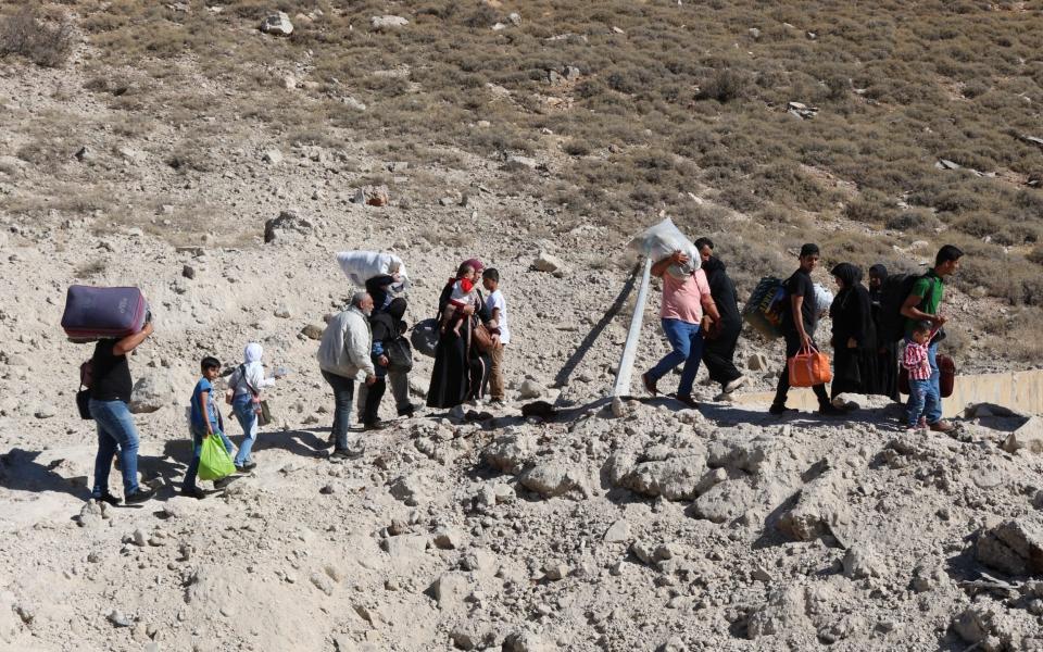 People fleeing Israeli bombardment in Lebanon walk around a crater caused by an Israeli strike near the Masnaa border crossing with Syria