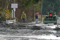 A tractor operator talks with people standing near a mud- and debris-covered road near Everson, Wash., Monday, Nov. 29, 2021. Localized flooding was expected Monday in Washington state from another in a series of rainstorms, but conditions do not appear to be as severe as when extreme weather hit the region earlier in November. (AP Photo/Elaine Thompson)