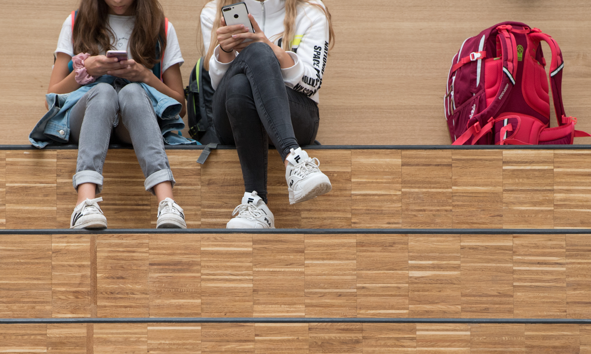 Two students sitting on bleachers using their phones