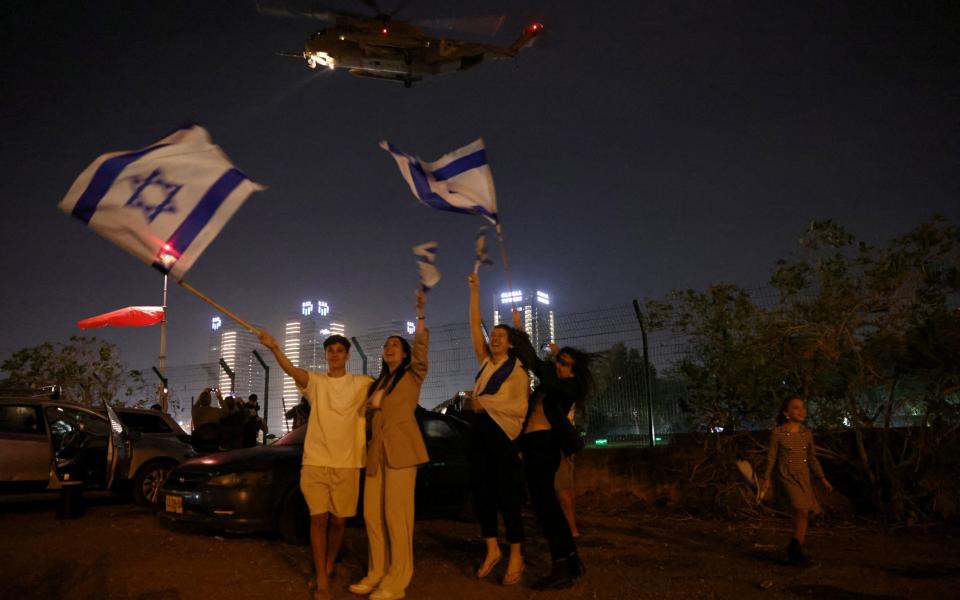 People wave Israeli flags as a helicopter, that was carrying hostages released as part of a deal between Israel and Palestinian Islamist group Hamas, departs from Schneider Children's Medical Center in Petah Tikva, Israel, November 24, 2023.