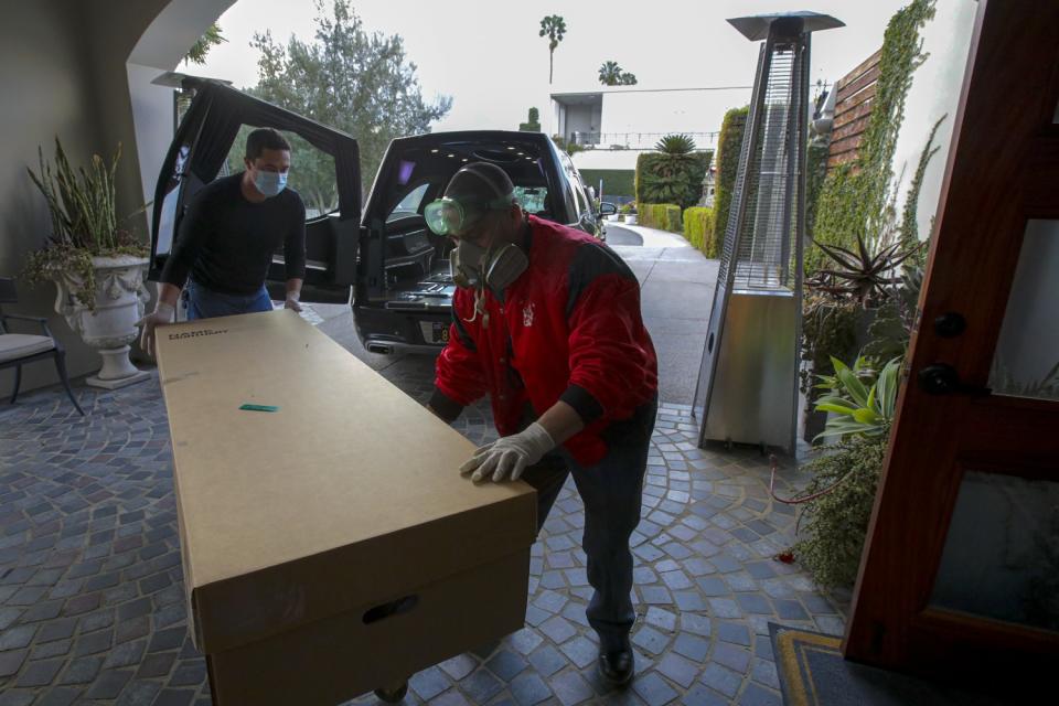 Two men wheel a cremation container away from a parked hearse.