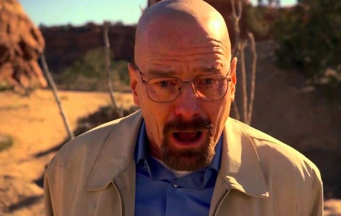 Walter White has teary eyes and a mouth open in shock; he is at an outdoor location with rocks and desert