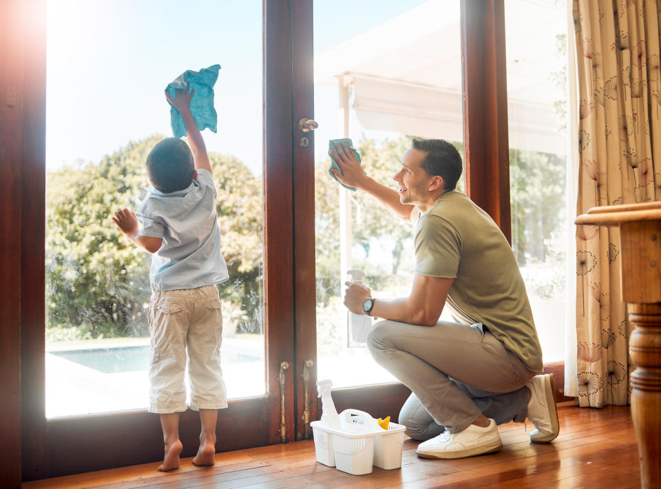 Little boy helping his father wash and wipe clean glass doors for household chores at home on a sunny day. Happy father and son doing spring cleaning together. Kid learning to be responsible by doing tasks