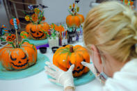 A woman, wearing a mask for protection against the COVID-19 infection, applies final decorations to Halloween themed sweets before they are shipped to customers at an upmarket deserts shop in Bucharest, Romania, Friday, Oct. 30, 2020. Romanians only started celebrating Halloween after the fall of the communist rule in 1989 and the feast's popularity kept growing every year. (AP Photo/Vadim Ghirda)