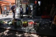 Vendor weighs fruits for a customer at his stall by the street outside a residential compound