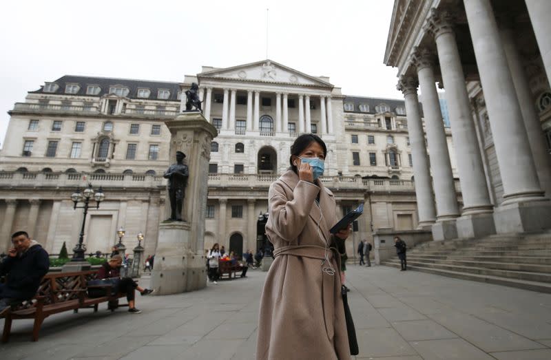 A woman, wearing a protective face mask, walks in front of the Bank of England, following an outbreak of the coronavirus, in London