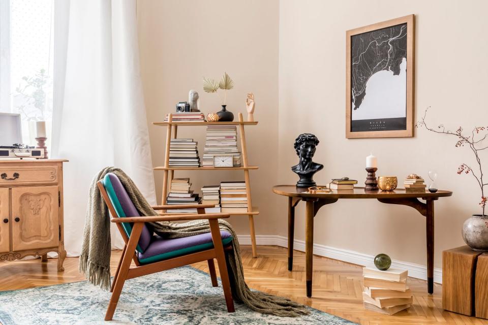 interior design of stylish library room with retro armchair, wooden table, bookstand, books, mock up poster map, vintage carpet and elegant personal accessories beige wall home decor template