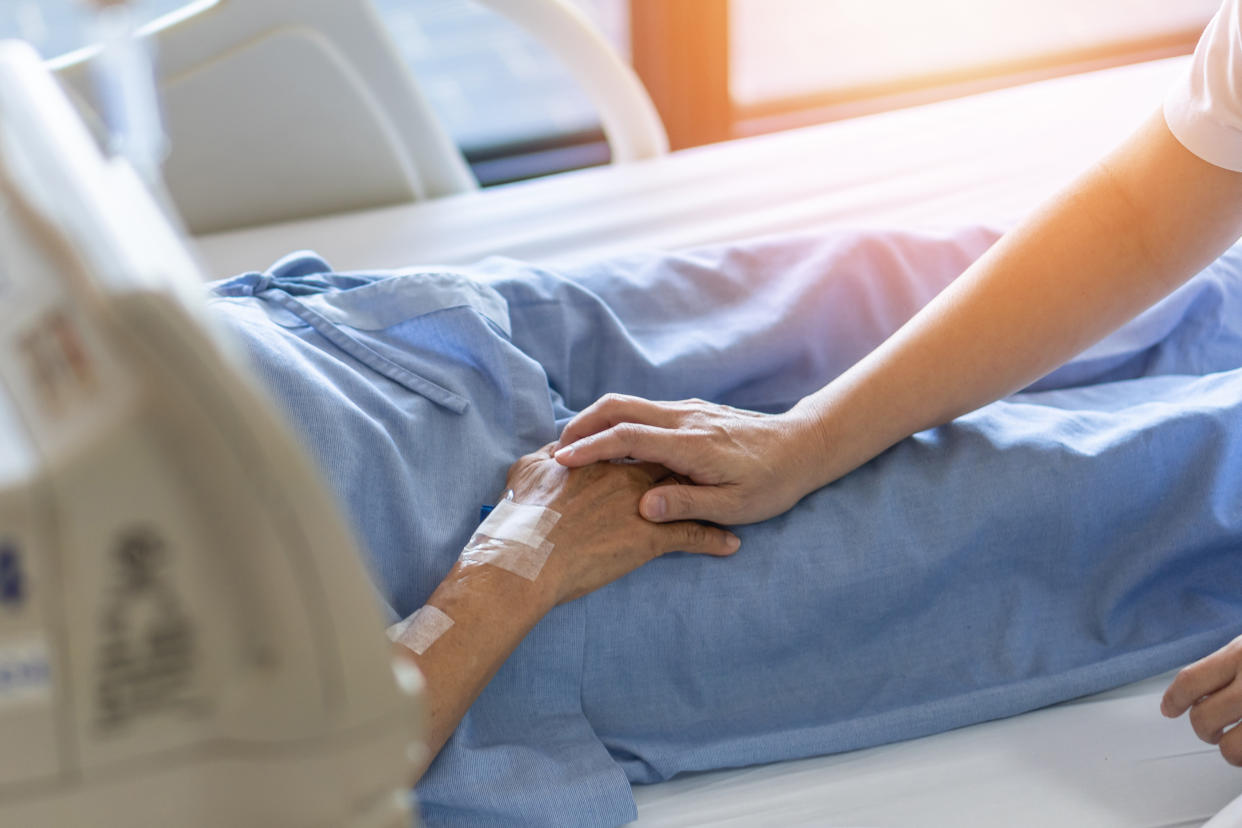 Caregiver tenderly holding the hand of an elderly patient in a hospital bed