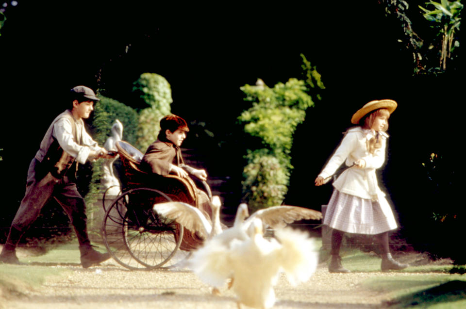 three children going through the garden with geese flapping their wings nearby