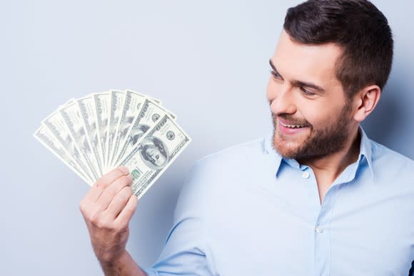 a man fans one-hundred-dollar bills in his hand and smiles as he looks at them.