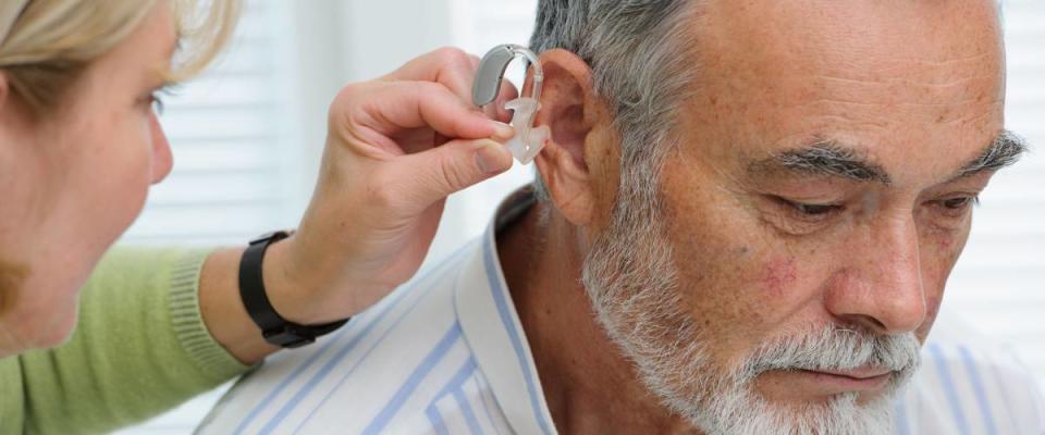 Doctor inserting hearing aid in senior's ear