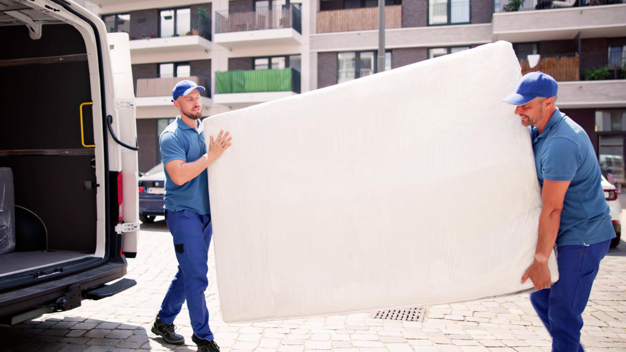  Two delivery men take a mattress that is being returned and carry it to a white van. 