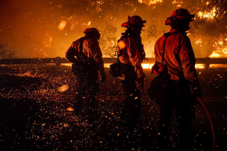 Firefighters turn to shield themselves from the ember wash as they battle the Bond Fire, started by a structure fire that extended into nearby vegetation, along Silverado Canyon Road on Thursday, December 3, 2020, in Silverado, California. / Credit: Kent Nishimura / Los Angeles Times via Getty