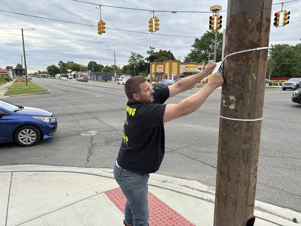 Suburban business owner William Shaw removes illegally posted signs Friday, June 28, 2024, in Detroit, from a street corner in as part of court-ordered community service. The city said that from February 2022 to July 2023, it removed more than 615 "Shaw's Plumbing" signs and he now is under court-order is serving community service removing illegally posted signs in the area. (AP Photo/Corey Williams)