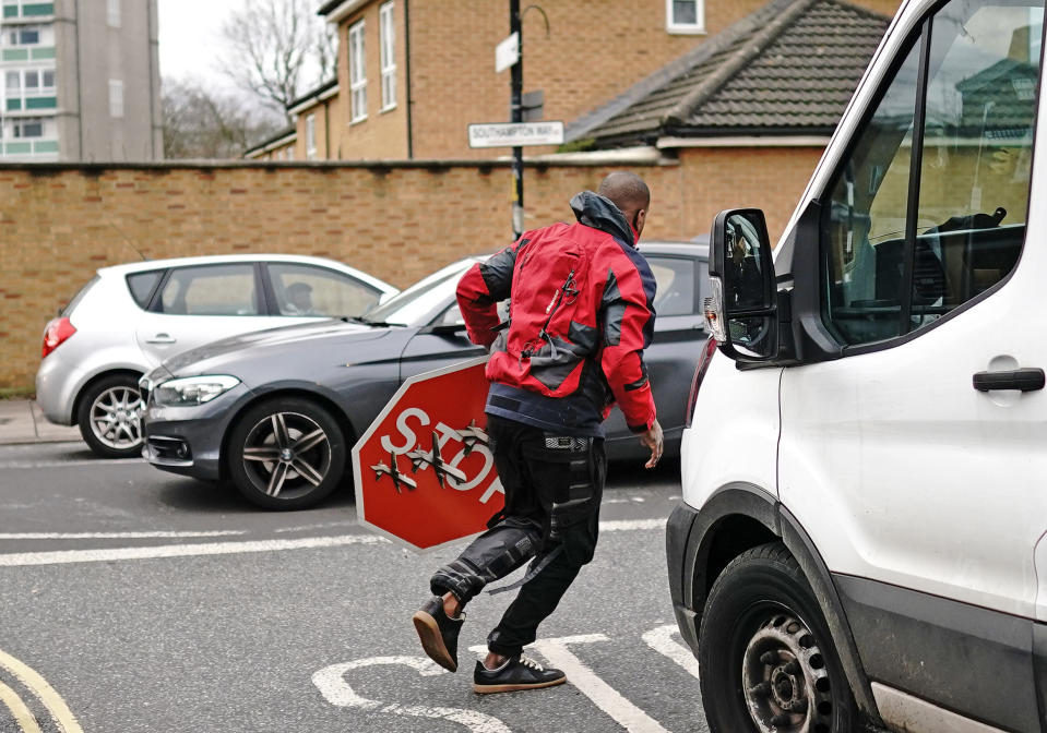 A person removes a piece of art work by Banksy, which shows what looks like three drones on a traffic stop sign, which was unveiled at the intersection of Southampton Way and Commercial Way in Peckham, south east London. Picture date: Friday December 22, 2023. (Photo by Aaron Chown/PA Images via Getty Images)