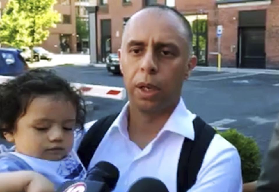 In this June 12, 2019, frame from video, Mayor Jorge Elorza holds his son Omar during a news conference about a shooting in Providence, R.I. Elorza's decision to frequently take his son to work with him has brought praise from some who say he's a role model, but also raised questions about whether he has taken it too far. (Steve Klamkin/WPRO News via AP)