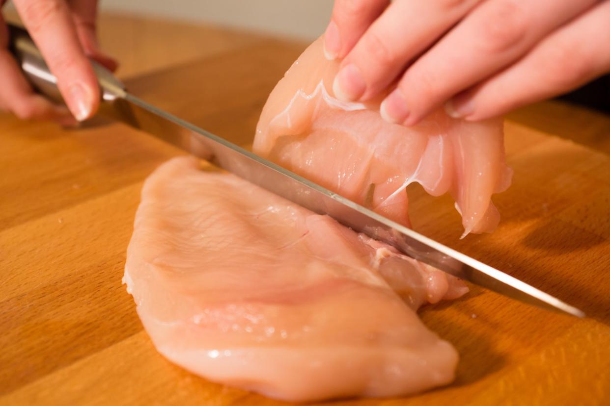 hands cutting chicken breast in half