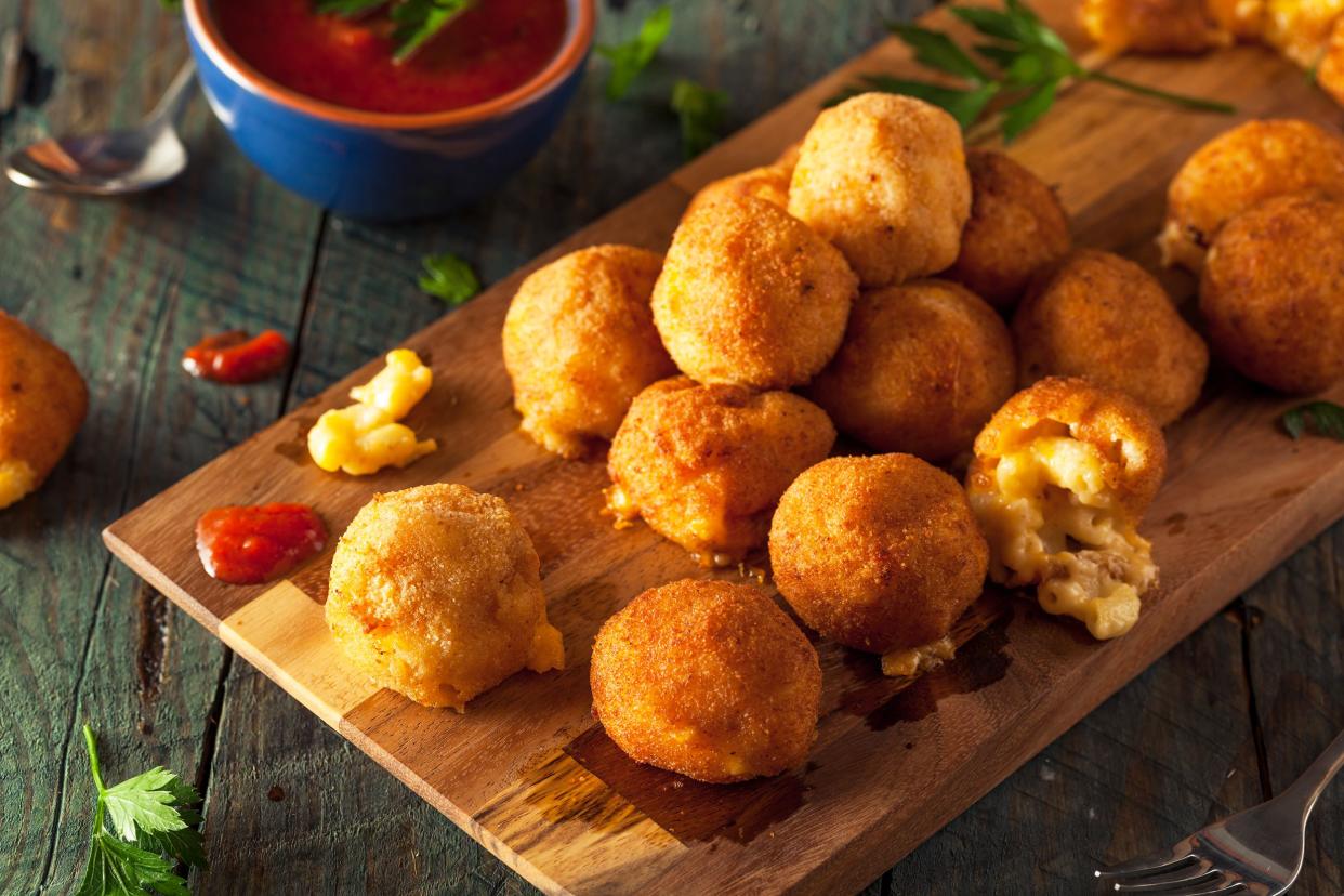Several homemade mac and cheese bites on an artistic wooden cutting board surrounded by ingredients