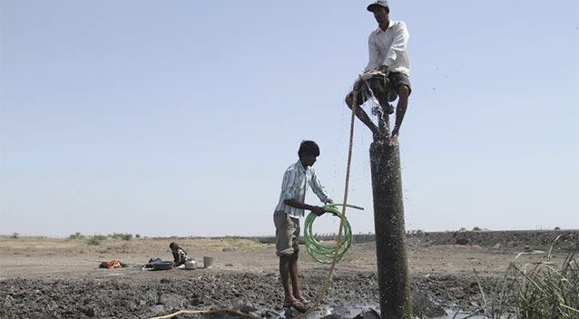 In this May 23, 2013 file photo, an Indian man sits on a leaking water pipe holding a pipe to fetch drinking water from it at Shiyal village near Bagodara, Gujart state, India. Photo: AP.