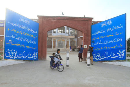 Children ride on a bicycle past the main gate of Government Islamic University, previously known as Jamia Al-Dawa Islamia, run by the Islamic charity organisation Jamaat-ud-Dawa (JuD) in Muridke near Lahore, Pakistan February 15, 2018. Picture taken February 15, 2018. REUTERS/Mohsin Raza