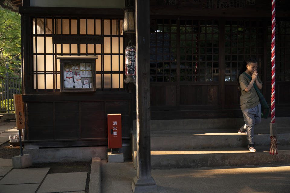 In this June 25, 2019, photo, a tourist visiting from Hong Kong prays at Gotokuji Temple in Tokyo. According to a centuries-old legend provided by the temple, Gotokuji, a Buddhist temple located in the quiet neighborhood of Setagaya, is the birthplace of beckoning cats, the famous cat figurines that are widely believed to bring good luck and prosperity to home and businesses. Some visitors come just to snap a few photos, while others make a trip to the temple to pray and make wishes. (AP Photo/Jae C. Hong)