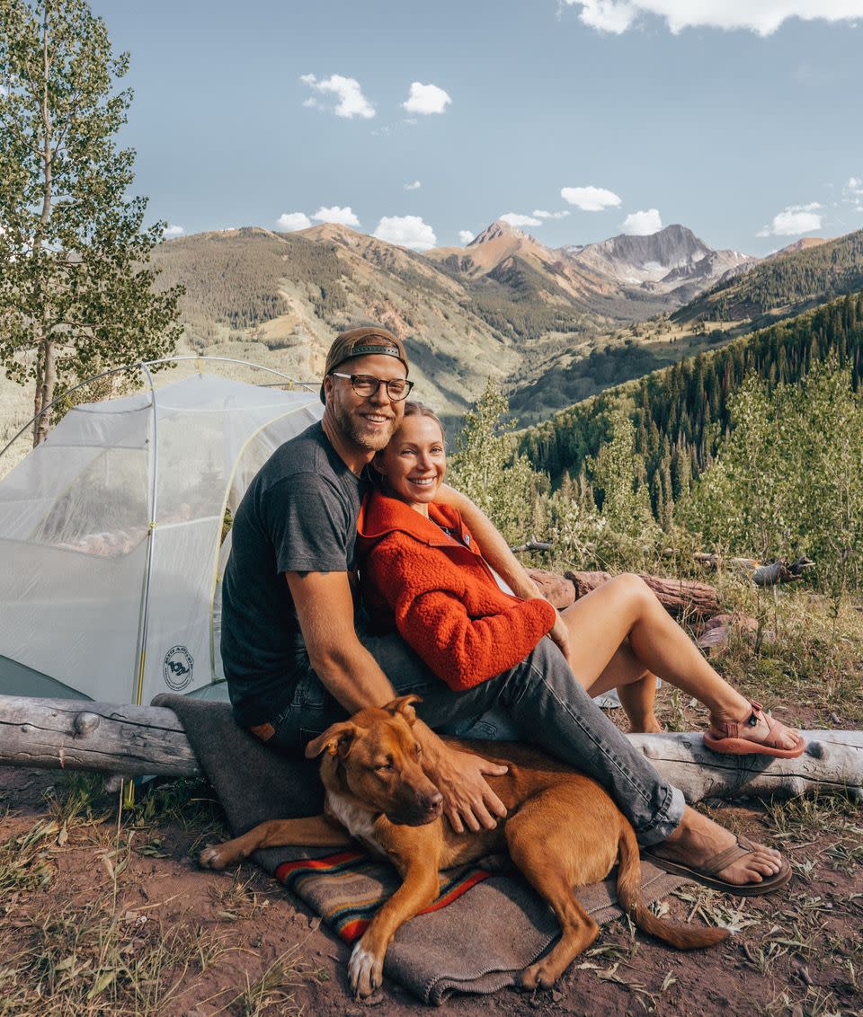sarah herron, husband, and dog in front of woodsy, mountainous landscape