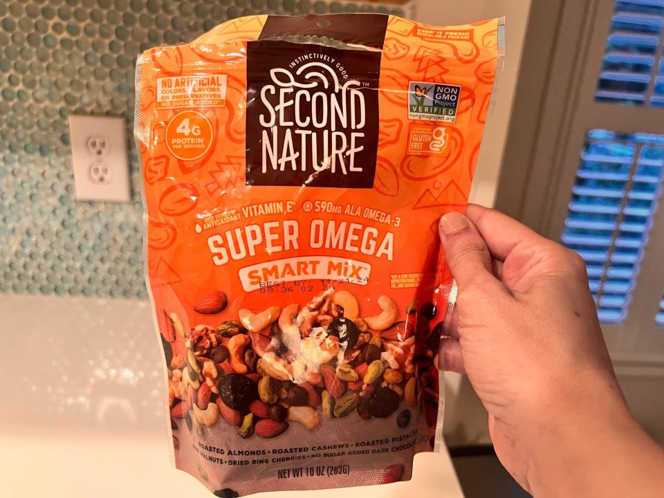 Die Hand hält eine Tüte mit Super-Omega-Snack-Mix von Second Nature hoch