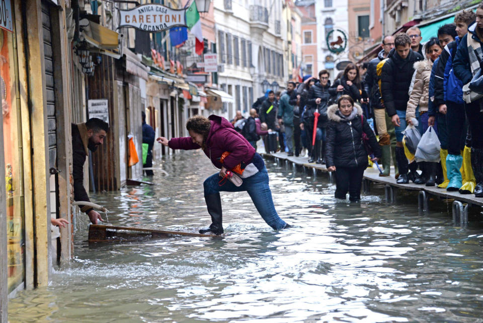 A woman tries to cross a flooded street as people walk on a trestle bridge during high water, in Venice, northern Italy, Friday, Nov. 15, 2019. Exceptionally high tidal waters returned to Venice on Friday, prompting the mayor to close the iconic St. Mark’s Square and call for donations to repair the Italian lagoon city just three days after it experienced its worst flooding in 50 years. (Andrea Merola/ANSA via AP)