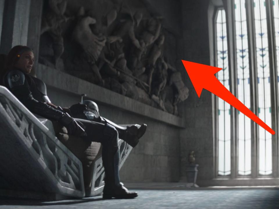 Bo-Katan sitting on a throne in front of a wall sculpture of Mandalorians fighting.