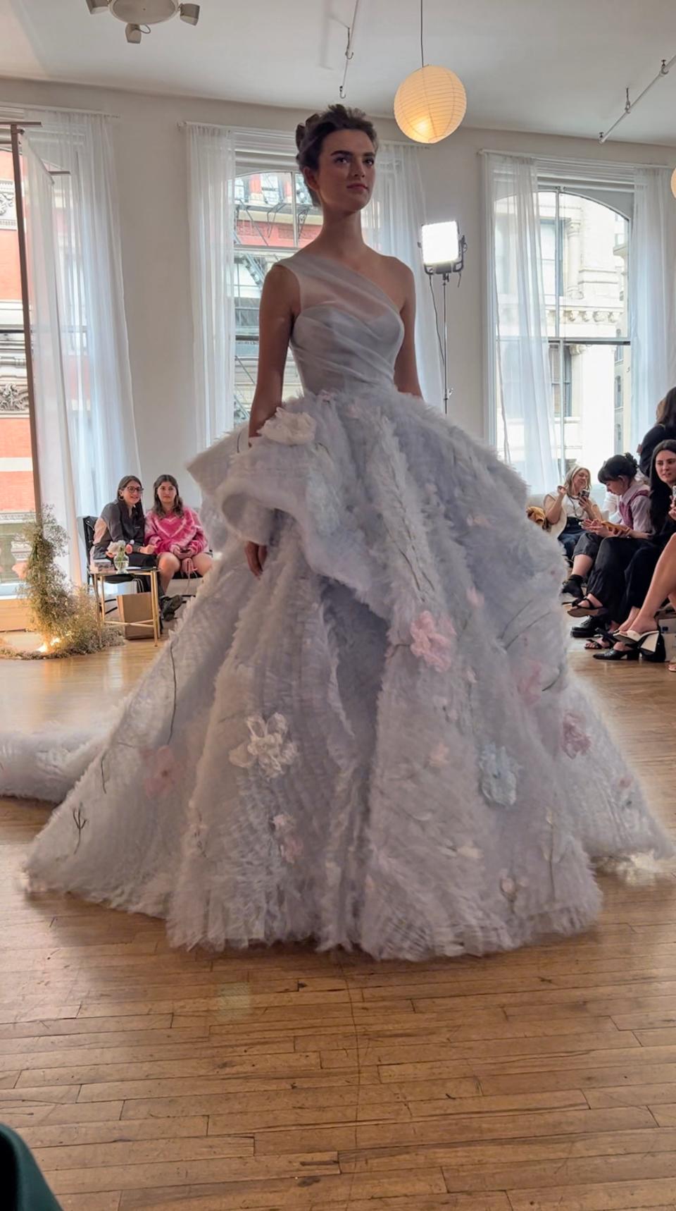 A woman poses in a blue wedding dress with a full skirt adorned with flowers.