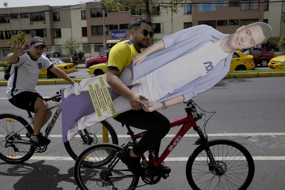 A supporter of Presidential candidate Daniel Noboa, of the National Democratic Action Alliance political party, carries a cardboard cutout of Noboa, as he bikes to attend a political rally in Quito, Ecuador, Wednesday, Oct. 11, 2023. (AP Photo/Dolores Ochoa)