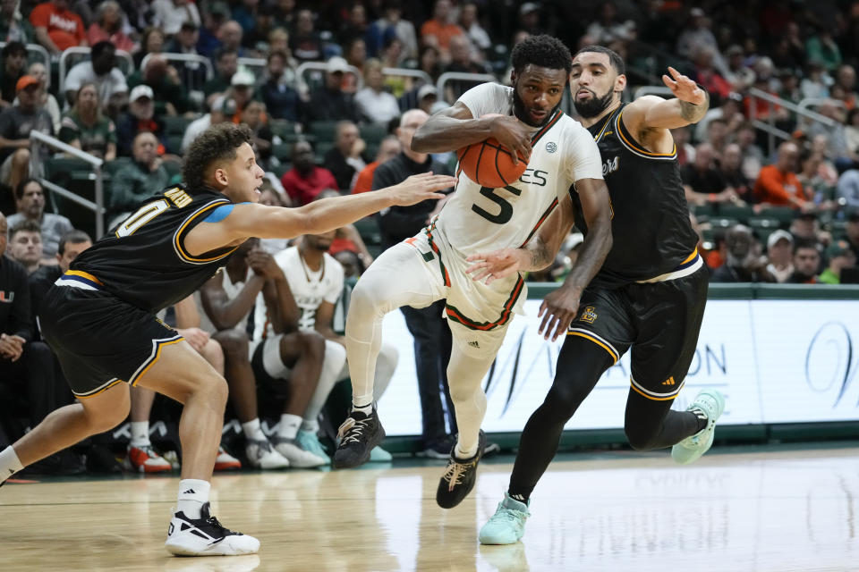 Miami guard Wooga Poplar (5) pushes through the defense of La Salle guard Andres Marrero (0) and La Salle guard Daeshon Shepherd during the second half of an NCAA college basketball game, Saturday, Dec. 16, 2023, in Coral Gables, Fla. Miami defeated La Salle 84-77. (AP Photo/Rebecca Blackwell)