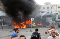 Syrians gather near a burning car in the coastal town of Tartus, Syria, where suicide bombers blew themselves up on May 23, 2016. Syrian TV reports said the bombings took place in a packed parking lot during morning rush hour. (SANA via AP)