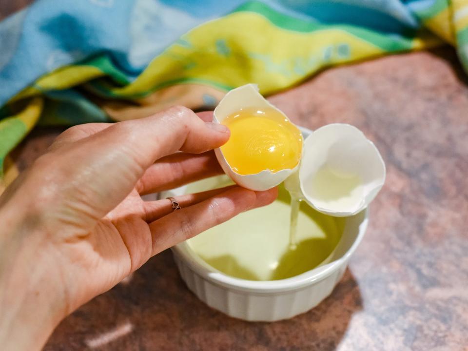 A hand cracking an egg in a ramekin.