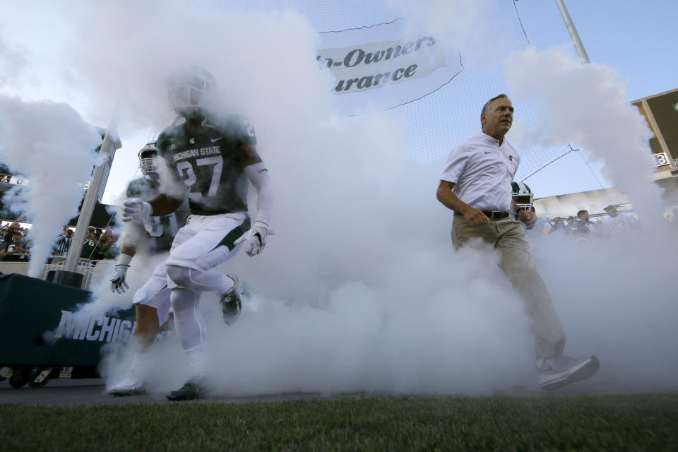 Michigan State's Khari Willis (27), Matt Sokol (81) and coach Mark Dantonio, right, run onto the field before an NCAA college football game against Utah State, Friday, Aug. 31, 2018, in East Lansing, Mich. (AP Photo/Al Goldis)