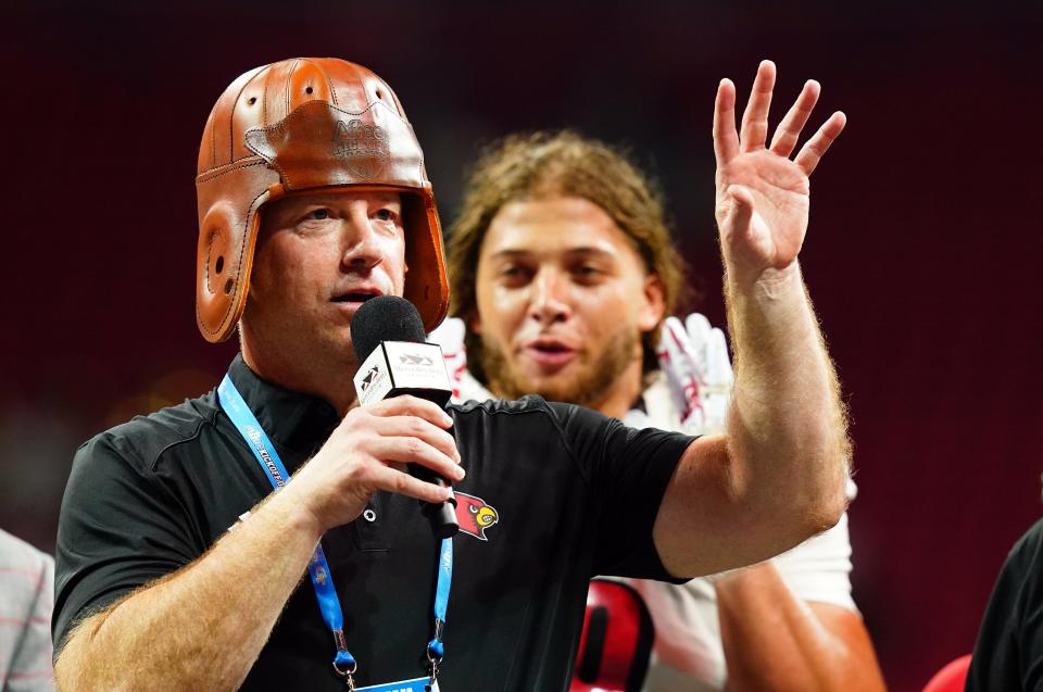 Louisville coach Jeff Brohm, wearing an old leather helmet given to the winner of the Aflac Kickoff Game, addresses the crowd after the Cardinals' win over Georgia Tech.