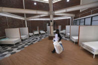 In this April 13, 2020, photo, a worker carries pillows as he walks in a room at a government building being prepared to become an emergency hospital for COVID-19 patients in Tangerang, Indonesia. While its neighbors scrambled early this year to try to contain the spread of the new coronavirus, the government of the world’s fourth most populous nation insisted that everything was fine. Only after the first cases were confirmed in March did President Joko Widodo acknowledge that his government was deliberately holding back information about the spread of the virus to prevent the public from panicking. The country now has the the highest death toll in Asia after China. (AP Photo/Tatan Syuflana)