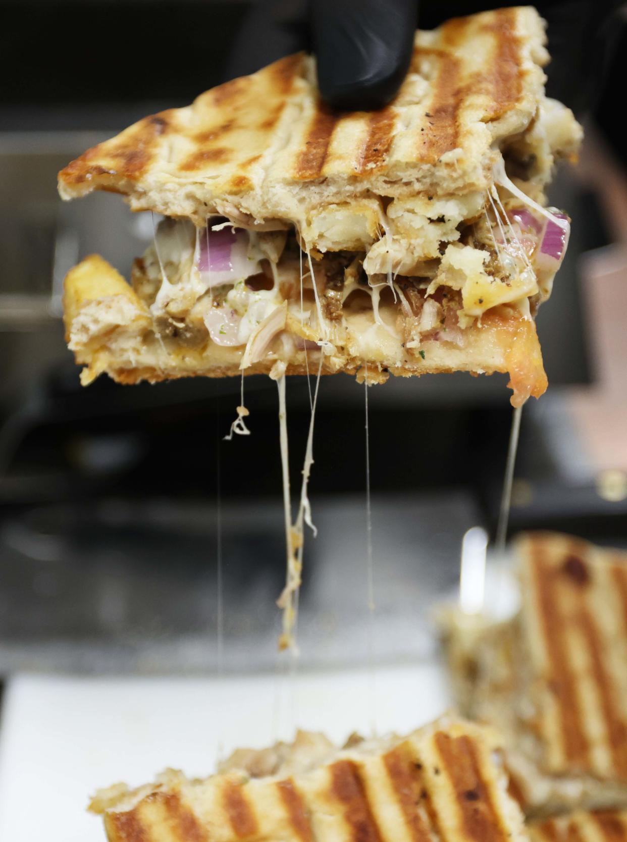 Employee Bobby Tran makes a skepasti at Grilla Greek Kouzina, 224 Broadway, Taunton, on Wednesday, April 3, 2024. The Greek-style club sandwiches are made with pita bread, onions, tomatoes, shredded cheese, hand-cut potatoes and chicken or pork.