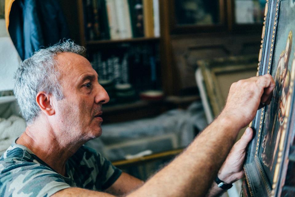 A senior restorer repairing an ancient canvas in his workshop