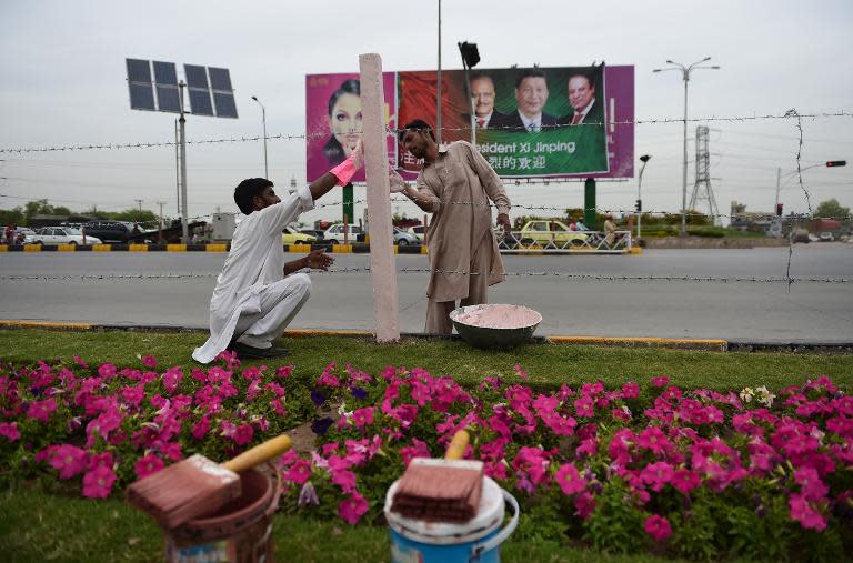 Local workers decorate the roadside in front of a billboard with pictures of Chinese President Xi Jinping, his Pakistani counterpart Mamnoon Hussain and Prime Minister Nawaz Sharif, in Islamabad, on April 18, 2015