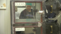 In this Nov. 20, 2019 image from video, Zach Ault retrieves bottled water through air-locked hatch inside a "metabolic chamber" where he is spending the night at the National Institutes of Health's hospital in Bethesda, Md. The airtight room allows scientists to measure how much oxygen is used and carbon dioxide is exhaled to figure out how much energy Ault's body is is using. (AP Photo/Federica Narancio)