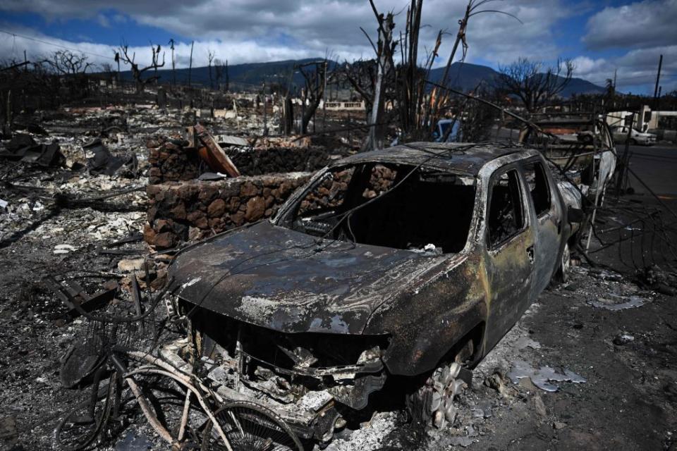 A burnt-out car lies in the driveway of a charred house in the aftermath of a wildfire in Lahaina, Hawaii.