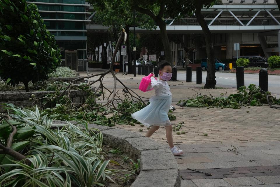 A girl walks past a fallen tree branches as the Hong Kong Observatory raised its No.8 storm warning, in Hong Kong, Saturday, July 2, 2022. Typhoon Chaba is buffeting Hong Kong, bringing high winds and plenty of rain, but no serious damage, as of midday Saturday. (AP Photo/Kin Cheung)