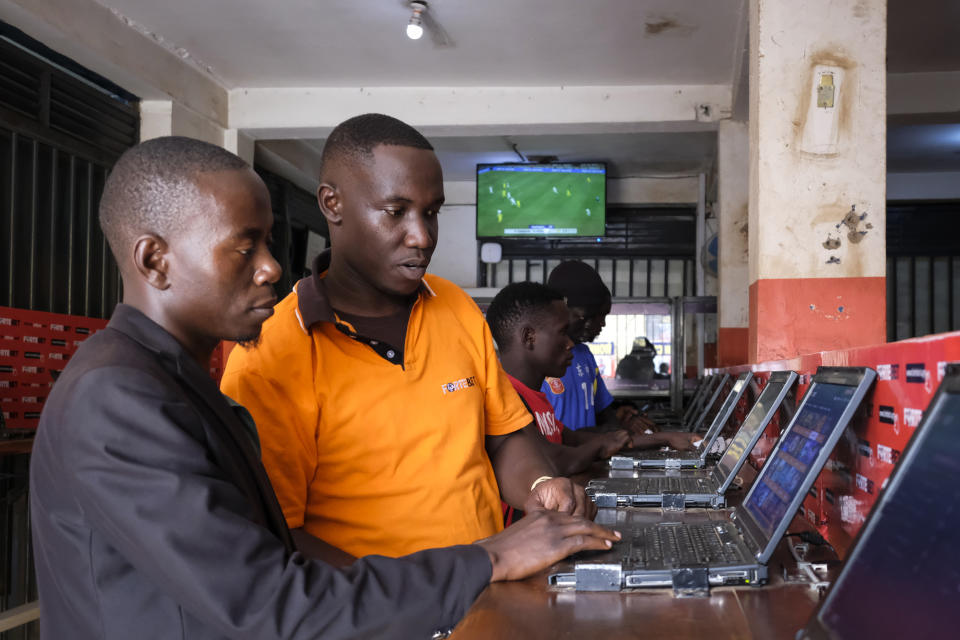 Shop manager David Mugisa, center, helps a customer at the Fortebet sports betting shop in the Ntinda area of the capital Kampala, Uganda, Tuesday, Dec. 6, 2022. In Uganda, an East African country where annual income per capita was $840 in 2020, many see sports betting as a path to survival and perhaps even prosperity. (AP Photo/Hajarah Nalwadda)