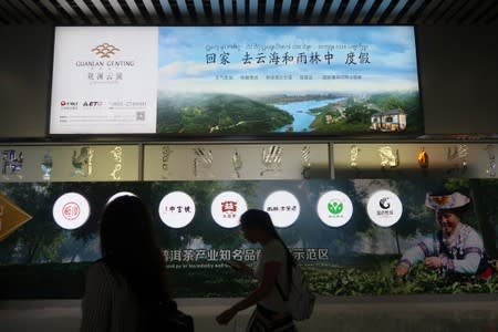 People walk past an advertisement of a property project at the airport in Xishuangbanna, Yunnan